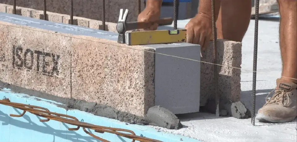 Close inspection of an Isotex first-course block aligned with a spirit level, with reinforcement and a pre-pour mortar bed visible.